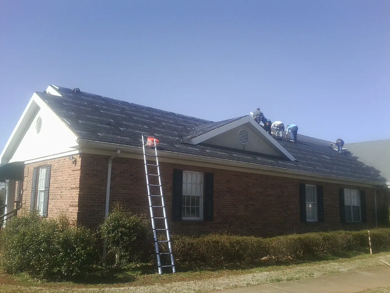 Crew tearing shingles off a brick ranch roof with a ladder set — Metal Roof Repair work by our crew in Loretto